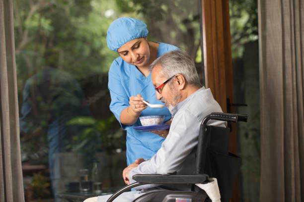 Female caregiver feeding food to disabled senior man on wheelchair